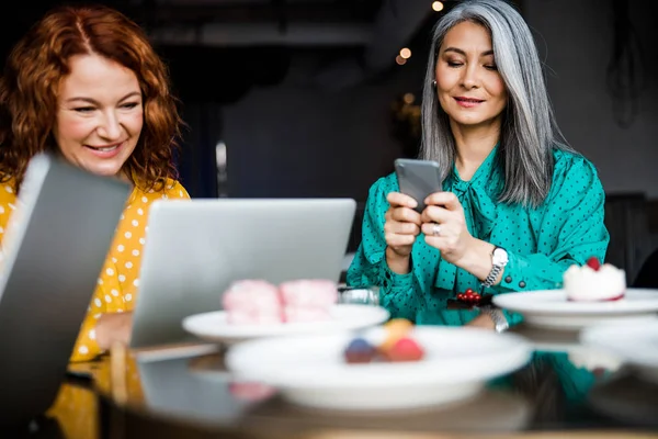 Charming women using laptop and cellphone in cafe — Stock Photo, Image