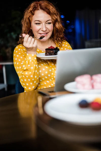 Lächelnde Dame, die Kuchen isst und Laptop benutzt — Stockfoto