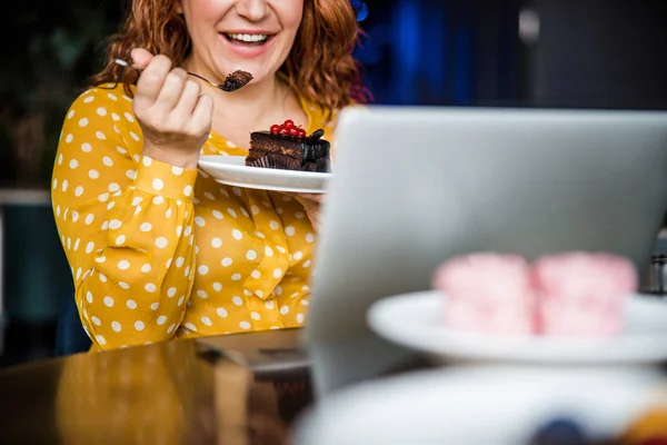 Fröhliche Frau isst Kuchen und benutzt Laptop — Stockfoto