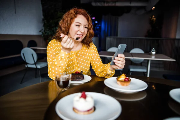 Charmante Dame isst Kuchen und benutzt Handy im Café — Stockfoto