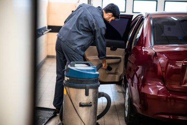 Elektrikli süpürge kullanan işçi tulumu giymiş.