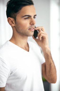 Genç adam evde akıllı telefondan konuşuyor.