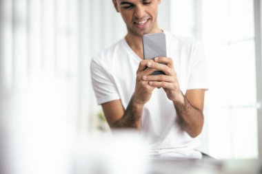 Happy young man using mobile phone in room