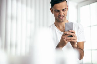 Smiling young man using mobile phone in room