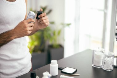 Tişörtlü adam evde deodorant kullanıyor.