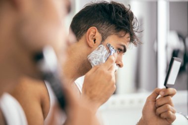 Evde tıraş olurken ayna tutan genç adam.