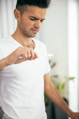 Genç adam banyoda diş fırçasına bakıyor.