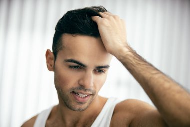 Gülümseyen adam saçını parmaklarıyla tarıyor.