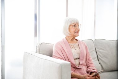 Kanepede oturan ve cep telefonu tutan neşeli yaşlı kadın.