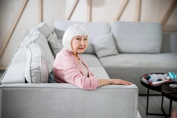 Старшая женщина сидит на удобном диване дома — стоковое фото