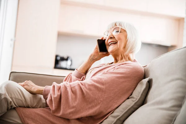 Весела стара жінка розмовляє на мобільному телефоні вдома — стокове фото
