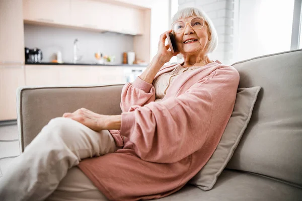 Усміхнена стара леді розмовляє на мобільному телефоні вдома — стокове фото