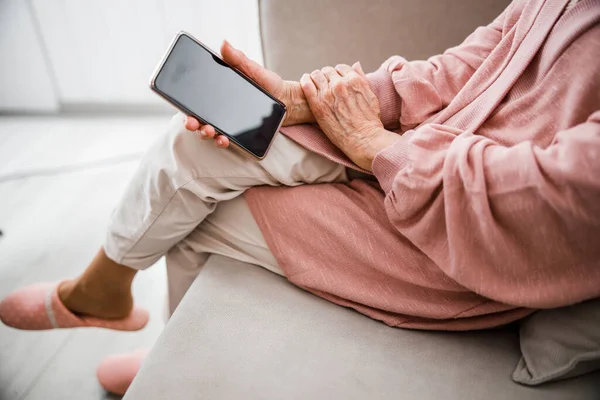 Gammal kvinna sitter på soffan och håller mobiltelefon — Stockfoto