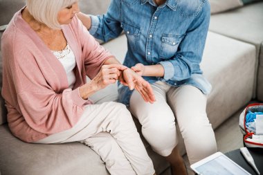 Kadın doktor yaşlı kadının hasta ellerini kontrol ediyor.