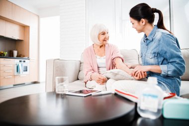 Aile doktoru, gülümseyen yaşlı kadının kolunu kontrol ediyor.