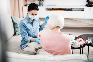 Kadın doktor yaşlı bayana iğne yapıyor.