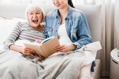 Neşeli yaşlı kadın yetişkin torunuyla kitap okuyor.