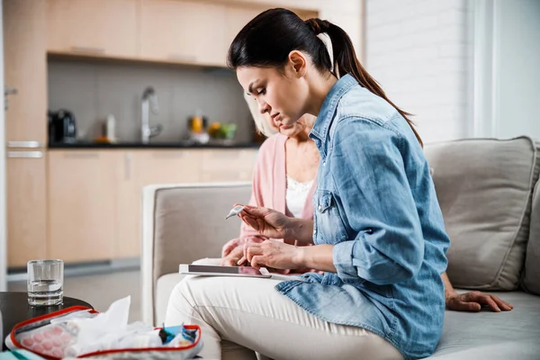 Mujer joven sosteniendo el termómetro y utilizando la tableta digital — Foto de Stock