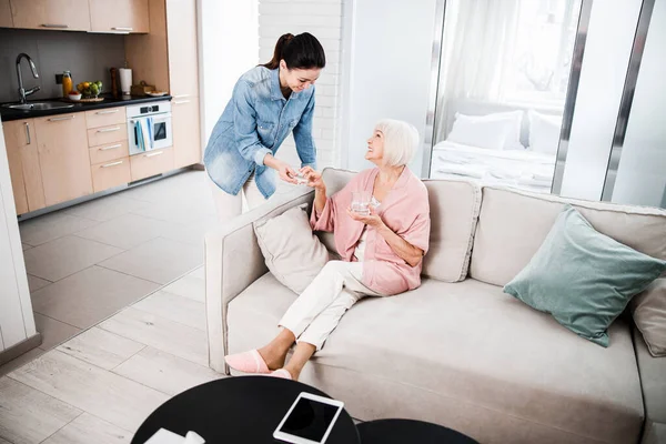 Cheerful young lady helping grandmother to take pills — Stock Photo, Image