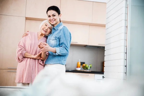 Smiling young lady hugging grandmother and holding her hand — Stock Photo, Image