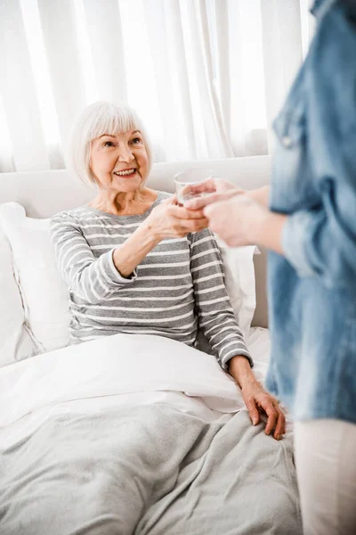 Young lady giving glass of water to elderly woman — Stock Photo, Image