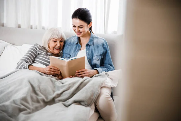 Happy grandmother and adult granddaughter reading book together — Stock Photo, Image