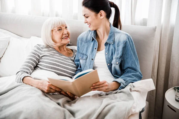 Alegre anciana leyendo libro con nieta adulta —  Fotos de Stock