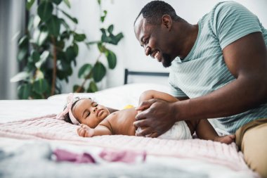 Afro-Amerikalı bir adam yeni doğmuş kızına bakıyor ve gülümsüyor.