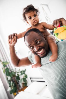 Neşeli Afro-Amerikan adam omuzlarında küçük bir kız taşıyor.