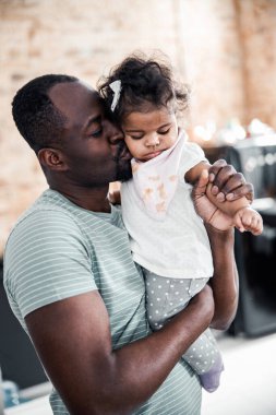 Afro Amerikalı bir adam yeni doğmuş kızını kucaklıyor ve yanağından öpüyor.