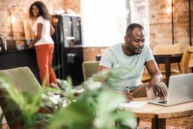 Evde dizüstü bilgisayarda çalışan Afro-Amerikalı bir adam.