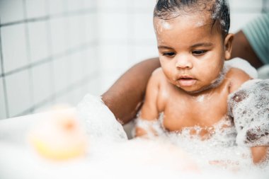 Afro American man bathing cute newborn child at home clipart