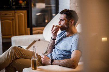 Delikanlı elinde içki olan bir pizza yiyor.