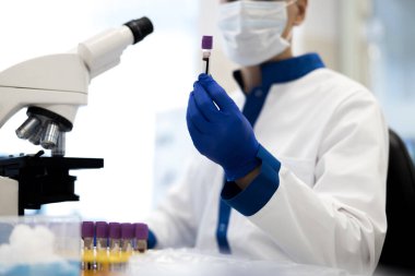 Erkek araştırmacı elinde kan örneğiyle laboratuvar tüpü tutuyor.