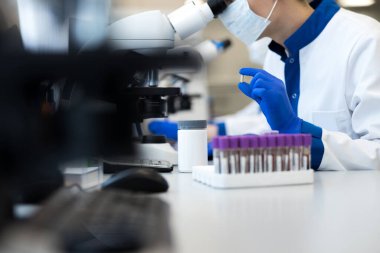 Erkek araştırmacı hap tutuyor ve mikroskop kullanıyor.