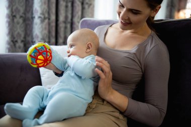 Küçük bebeğiyle oturma odasındaki kanepede oynayan mutlu kadın.