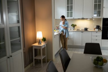 Mutlu anne bebeğiyle mutfakta duruyor.