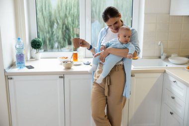 Mutlu güzel anne bebeğiyle sıcak bir içecek tutuyor.