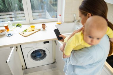 Güzel anne bebeğiyle çamaşır makinesinin yanında duruyor.