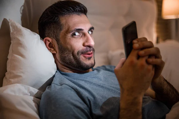 Смешной парень с мобильным телефоном в спальне фото акции — стоковое фото