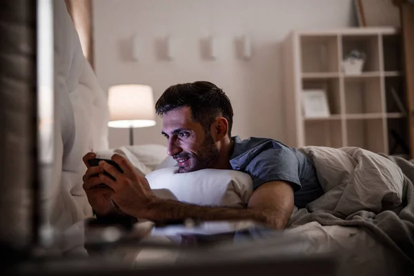Wesoły człowiek relaksujący się z telefonu komórkowego w sypialni stock photo — Zdjęcie stockowe