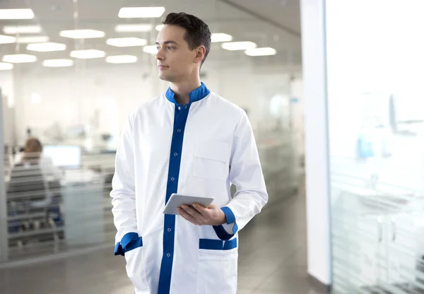 Guapo joven en bata de laboratorio sosteniendo gadget moderno — Foto de Stock