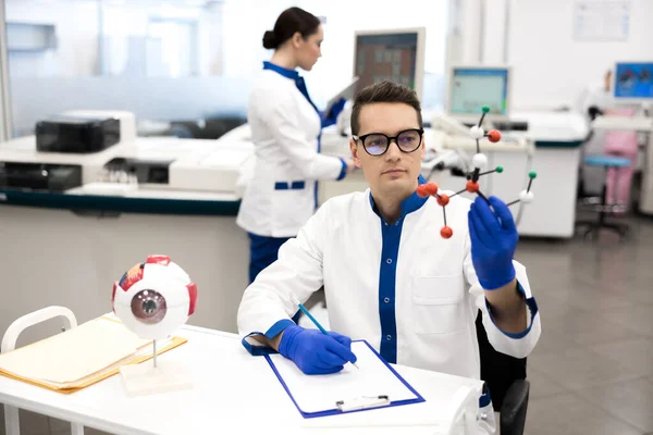 Científico investigador en bata de laboratorio mirando el modelo de molécula — Foto de Stock