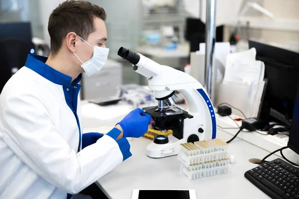 Wetenschapper in medisch masker met behulp van microscoop in laboratorium — Stockfoto
