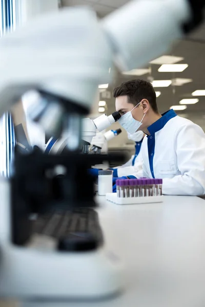 Wetenschapper op zoek in de microscoop tijdens het werken aan medisch onderzoek — Stockfoto