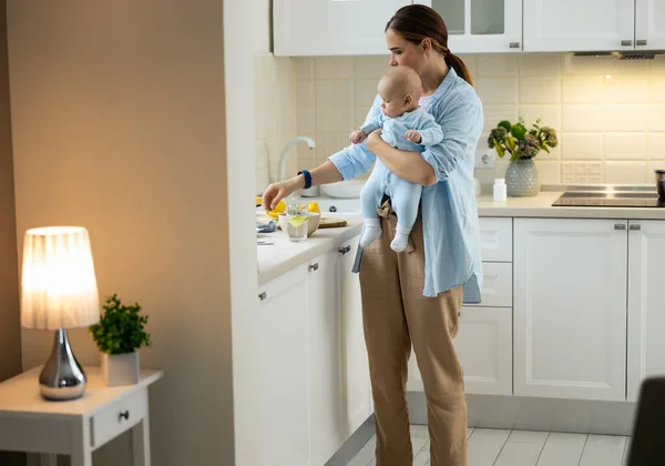Mujer feliz sostiene a su bebé en la cocina —  Fotos de Stock