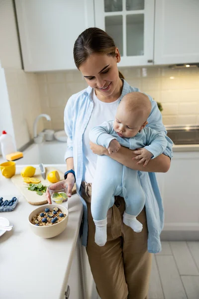Uśmiechnięta dama stojąca z dzieckiem w kuchni w domu — Zdjęcie stockowe