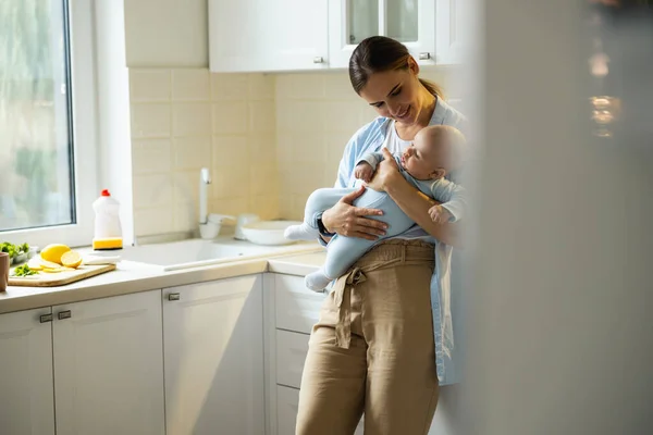 Fiatal anya pihen a gyerekével a konyhában. — Stock Fotó