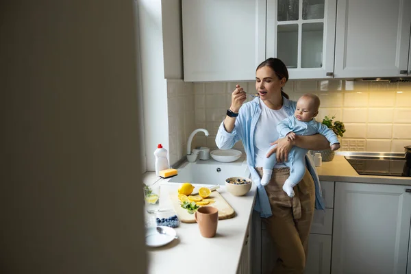 Boldog gyönyörű anya kezében baba és eszik zabpehely — Stock Fotó