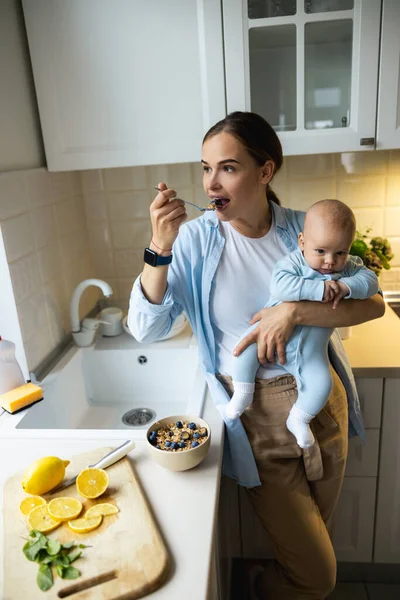 Glad vacker kvinna som håller i barnet och äter havregryn — Stockfoto